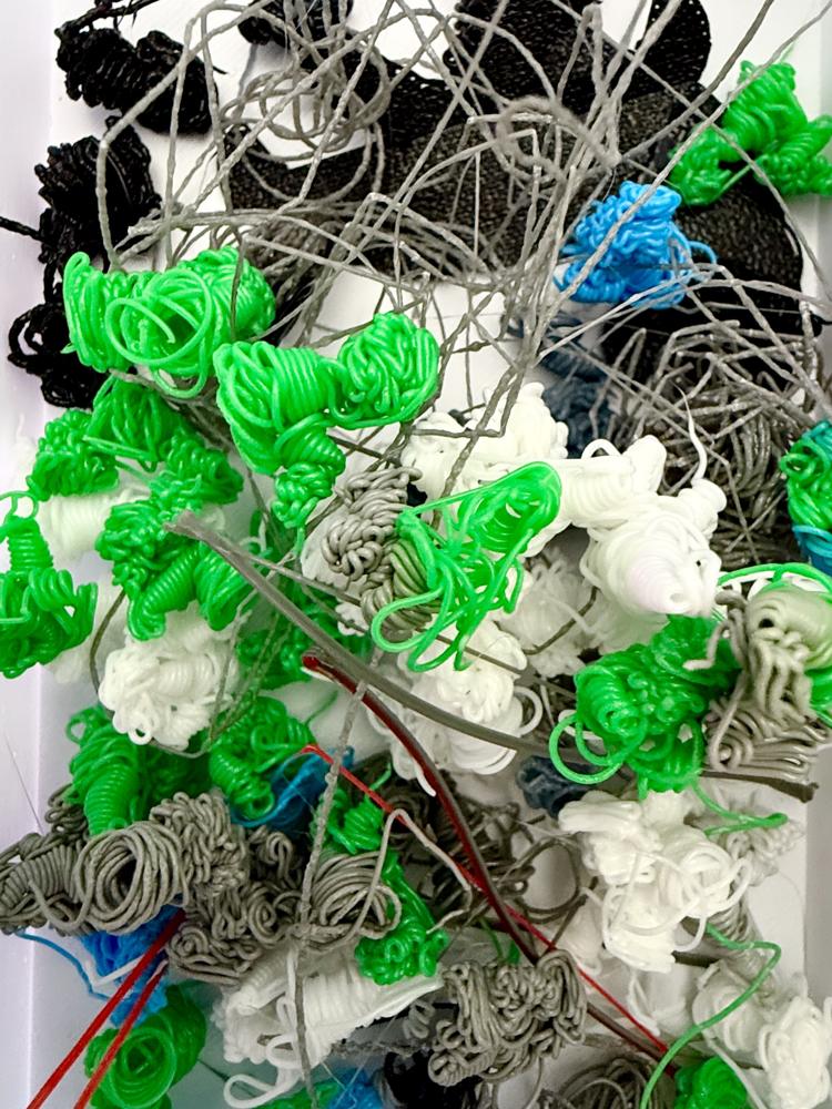 Scarti di filamento verde, bianco, grigio e nero prodotti dai cambi colore della stampa 3D multicolore